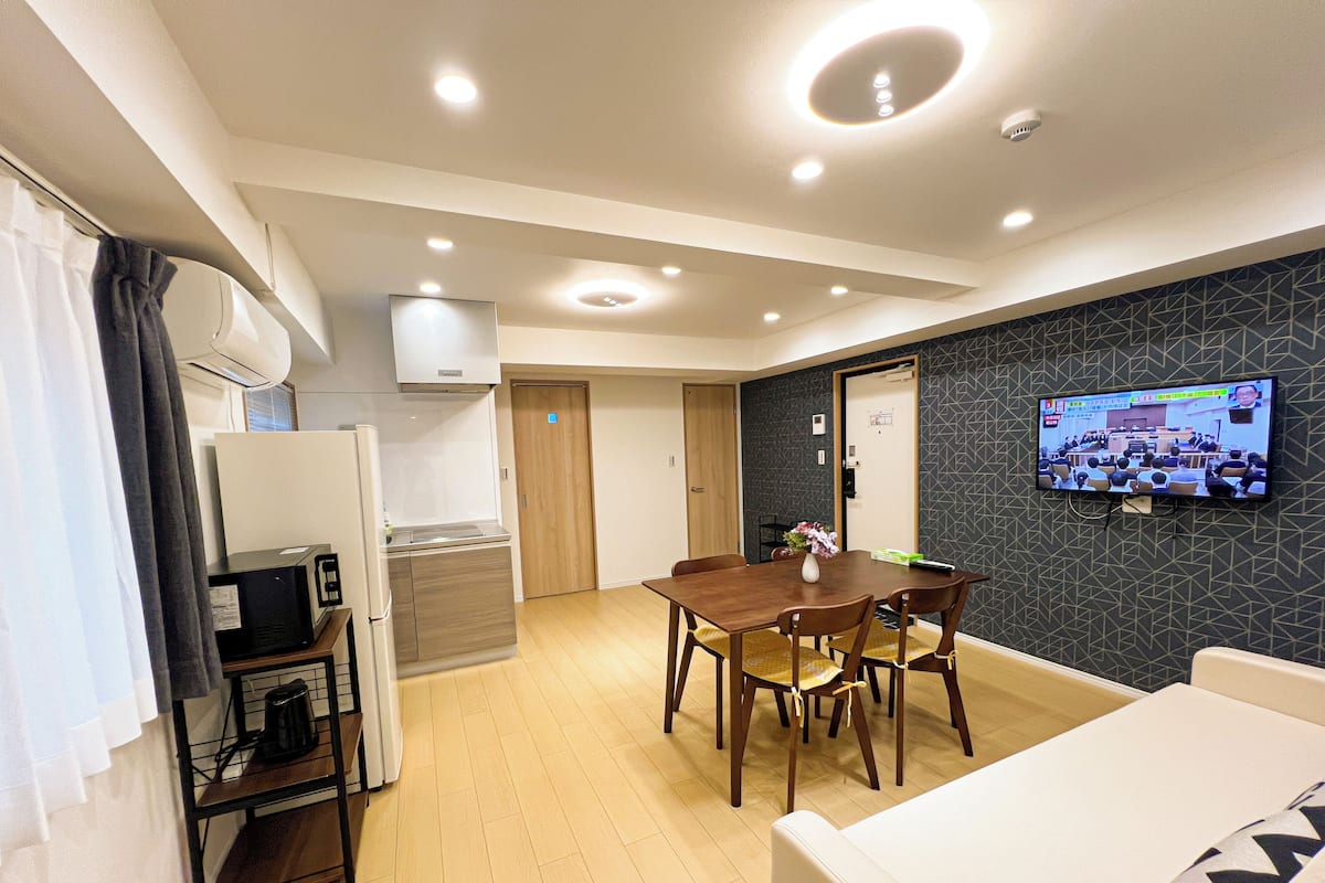 Une chambre d’hôtel moderne dotée d’un coin repas, d’un téléviseur fixé au mur et d’une kitchenette.