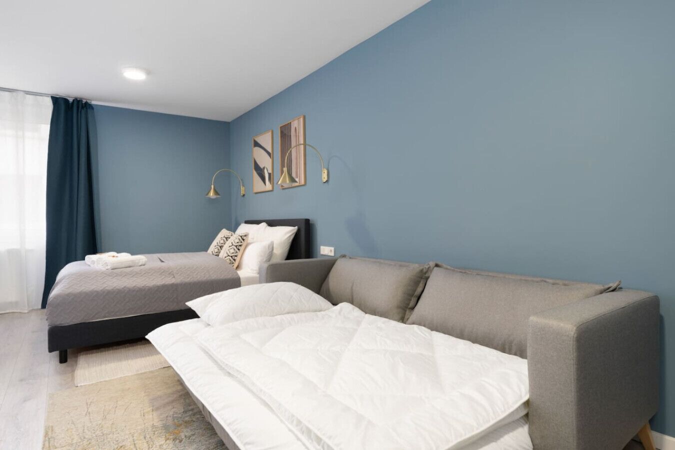 A modern bedroom with a bed, a sofa, and a large window with curtains.