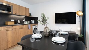Een moderne keuken met houten kastjes, een ingebouwde magnetron en een wasmachine. Een eettafel met borden, glazen en een vaas is gedekt voor een maaltijd.