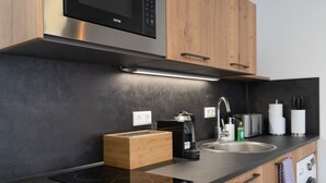 Een moderne keuken met een ingebouwde magnetron, koffiezetapparaat, spoelbak en houten kasten.