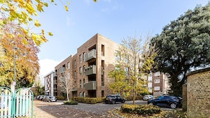 A multi-story residential building with balconies, a parking area, and a tree-lined street. - Chic Crystal Palace Flat with Balcony & Workspace (London)