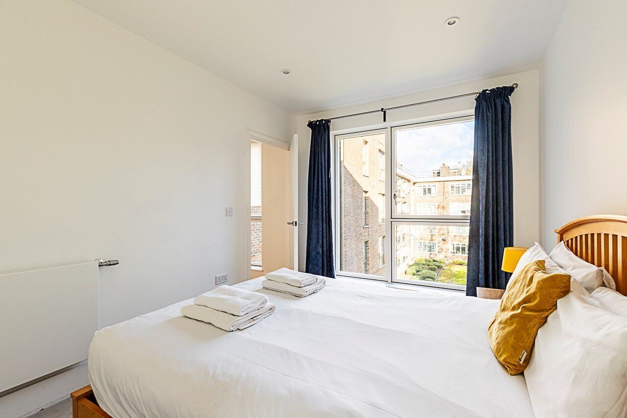 A hotel room with a large bed, a view of the city through a window, and a wooden headboard.