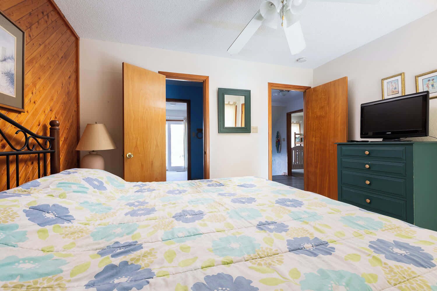 A bedroom with a bed, a dresser, a television, and a ceiling fan.