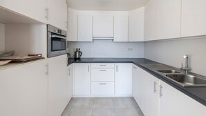 A modern kitchen with white cabinets, a black countertop, stainless steel appliances, and a double sink. - Seaview Apartment on the Beach - Free Parking (Ostend)