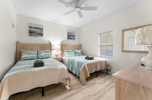 Ein Schlafzimmer mit zwei Betten, einem Deckenventilator, Bildern an den Wänden und einem Fenster mit Jalousien.