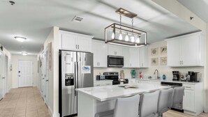 A modern kitchen with white cabinets, stainless steel appliances, a central island with bar stools, and a hanging light fixture.