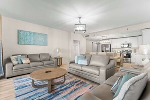 Ein modernes Wohnzimmer mit einer Sofagarnitur, einem Couchtisch und einer Küchenzeile im Hintergrund.