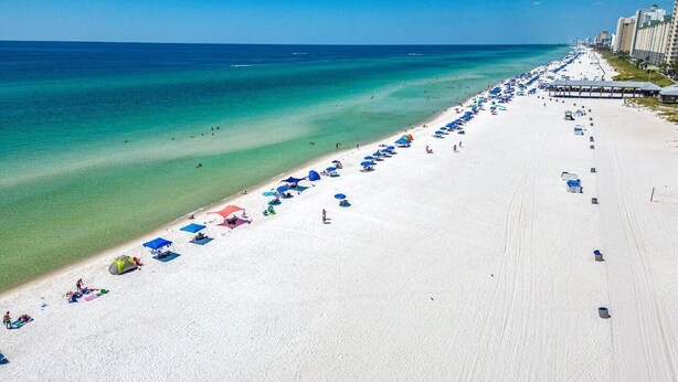 A beach with rows of umbrellas and beach chairs, a clear blue sky, and a calm sea.