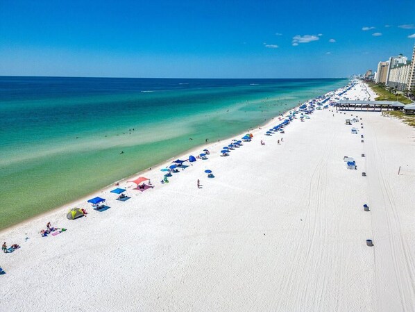Ein Strand mit Reihen von Sonnenschirmen und Liegestühlen, einem klaren blauen Himmel und ruhiger See.