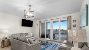 A modern living room with a sofa, a coffee table, a TV, and a balcony with a view.