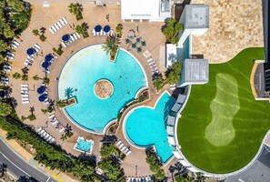 Ein Luftbild eines Resorts mit einem zentral gelegenen Schwimmbecken, Liegestühlen und einem gepflegten Rasen.