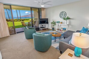 A living room with a TV, sofa, chairs, and a view of the ocean. - Koa Lagoon #105 Ground Floor Ocean View, 1BD/1BA, Sleeps 4 (Kihei)