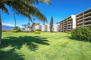 A hotel with a well-maintained lawn, palm trees, and a clear view of the mountains in the background. - Koa Lagoon #105 Ground Floor Ocean View, 1BD/1BA, Sleeps 4 (Kihei)