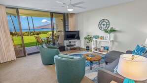 A living room with a TV, sofa, chairs, and a view of the ocean. - Koa Lagoon #105 Ground Floor Ocean View, 1BD/1BA, Sleeps 4 (Kihei)