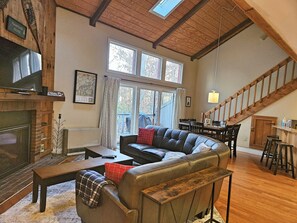 A spacious living room with a leather sofa, a fireplace, and a dining area with wooden furniture. - Fireplace, ski shuttle, pool & hot tub access. L3205 by LRS (Lincoln)