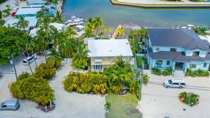 An aerial view of a coastal property with a large house, a swimming pool, and several parked cars.