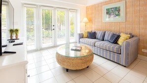 A living room with a sofa, a glass coffee table, a TV, and a door with blinds. - Sundance: Ocean View, Dock, Pool, Elevator, Beach, Kayaks, Ice Machine (Marathon)