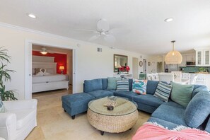A living room with a blue sectional sofa, a round woven coffee table, and a ceiling fan. - Sundance: Ocean View, Dock, Pool, Elevator, Beach, Kayaks, Ice Machine (Marathon)