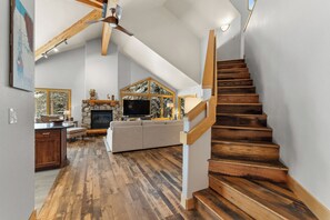 Un vaste espace de vie doté d’une cheminée, d’un grand téléviseur et d’un escalier en bois.