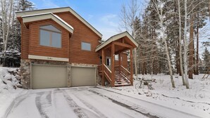 A wooden cabin with a garage, a covered porch, and a staircase leading to the entrance.