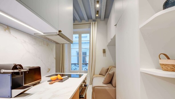 Een compacte keuken met een modern ontwerp, met een ingebouwde oven, een aanrecht met een snijplank en oranje details, en een uitzicht op een balkon door een raam.