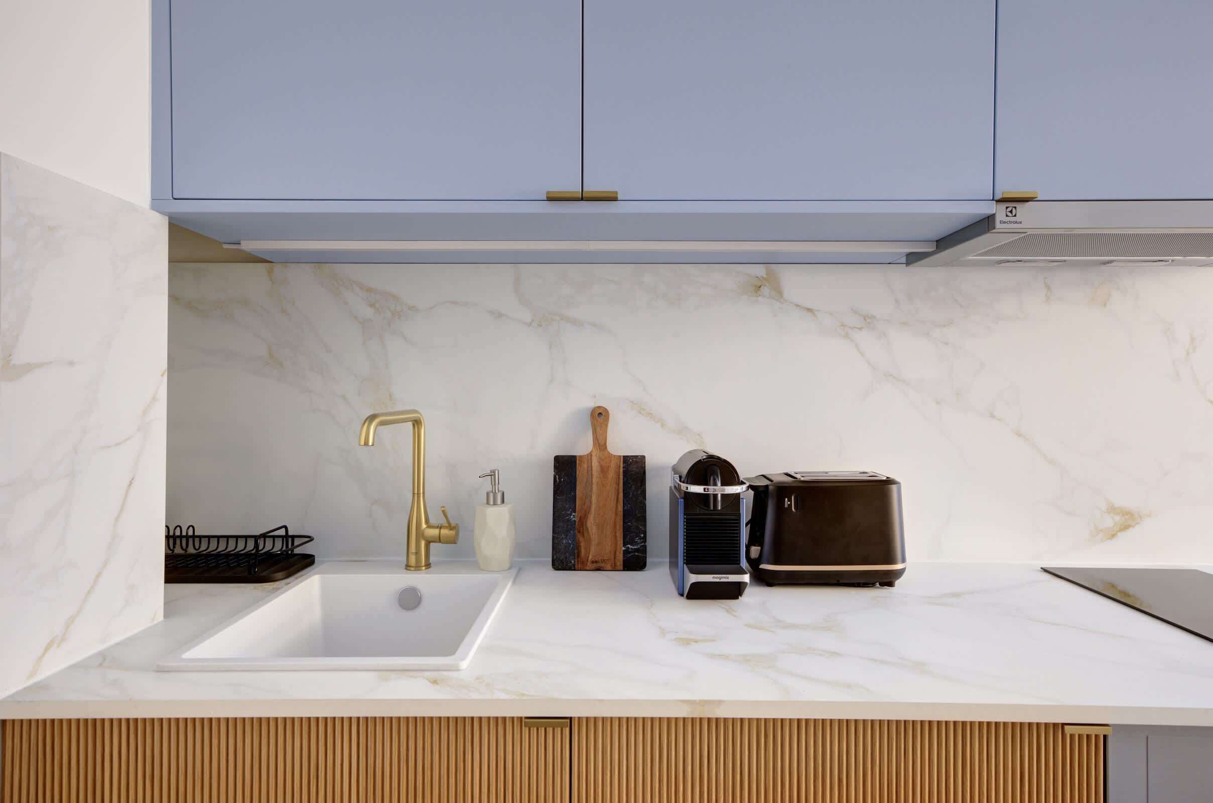 A kitchen with a white marble countertop, a gold faucet, a toaster, and a wooden cutting board.