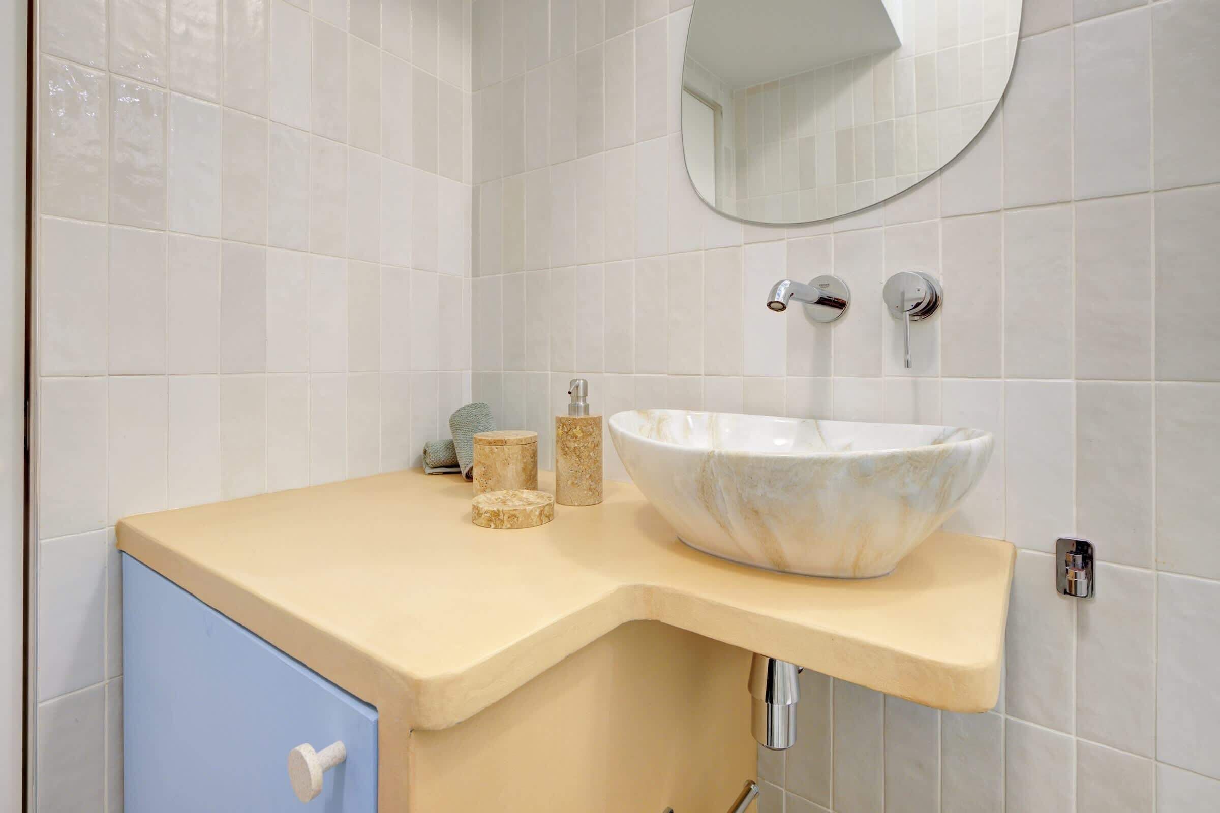 Een badkamer met een beige aanrecht, een grote wastafel, een blauwe kast en een spiegel boven de wastafel.