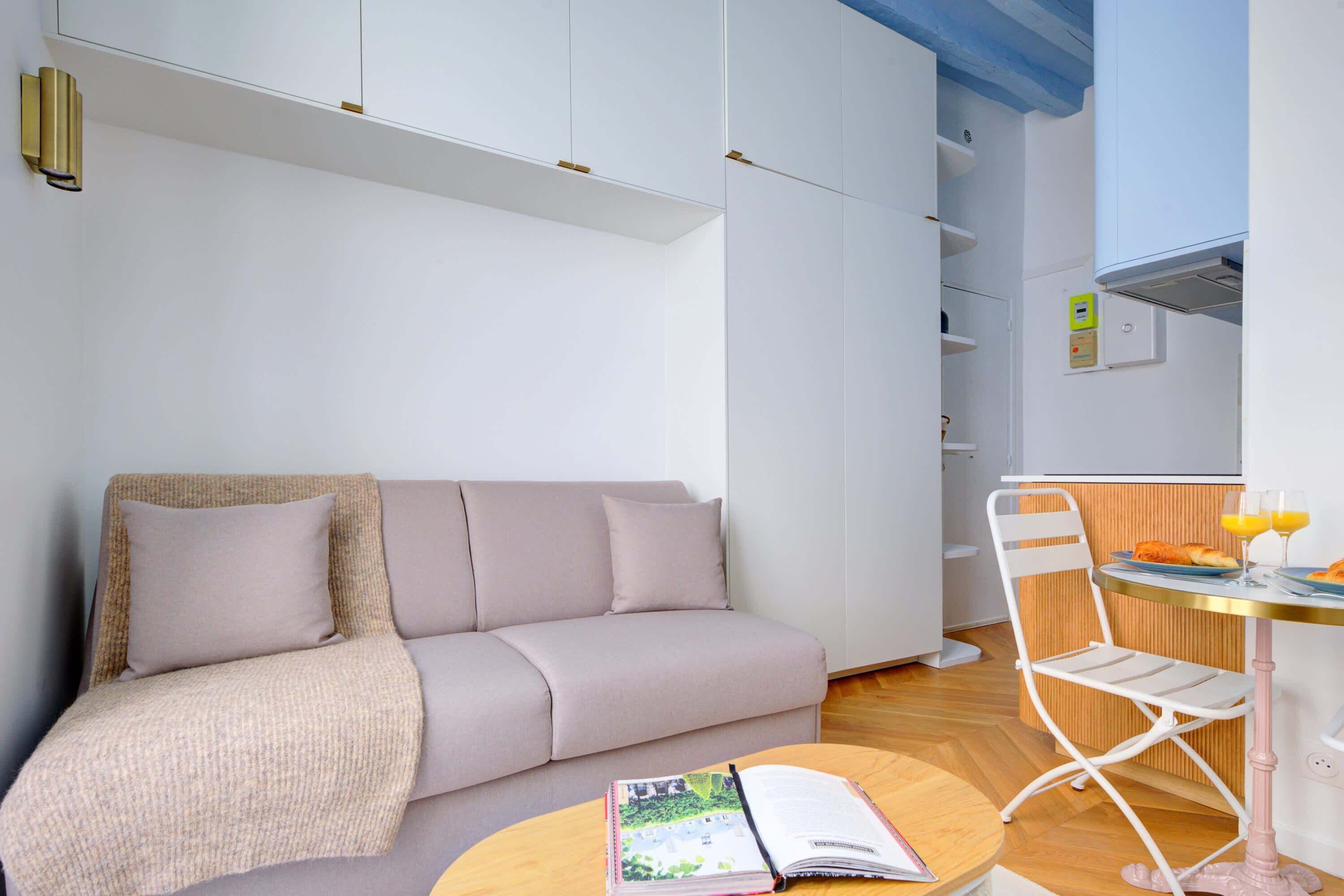 A modern living room with a sofa, a coffee table with a book, and a dining area with a table and chairs.