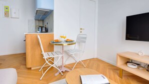 Een compacte keuken met een moderne kookplaat, een kleine eettafel met twee stoelen, en een flatscreen televisie aan de muur bevestigd.