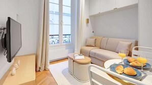 Een moderne hotelkamer met een bank, ontbijtplateau en een televisie.