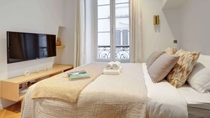 Een slaapkamer met een bed, een televisie, een raam en een nachtkastje.