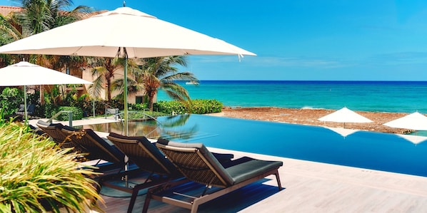 A poolside area with lounge chairs and umbrellas, overlooking a beach and ocean.