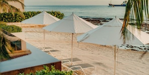 A beachside area with white umbrellas, lounge chairs, and a view of the ocean.