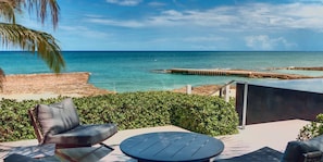 A patio with a view of the ocean, a chair, a table, and a small structure.