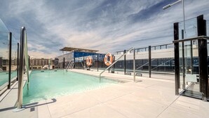 Une piscine sur le toit, avec de l’eau claire, des rampes en métal et des panneaux indiquant les consignes de sécurité relatives aux bouées de sauvetage.