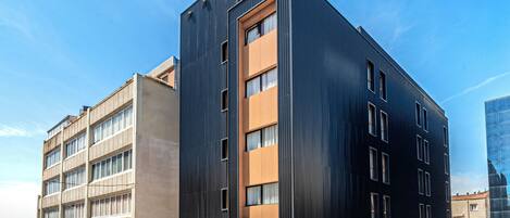 A modern multi-story building with a mix of dark and light facades, featuring large windows and a flat roof.