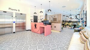 Un hall d’hôtel moderne comprenant un comptoir d’accueil, des ascenseurs et un espace détente avec des tables et des chaises.