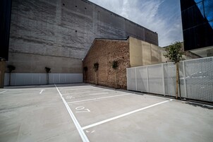 An empty parking lot with numbered parking spaces and a brick wall with a metal fence.