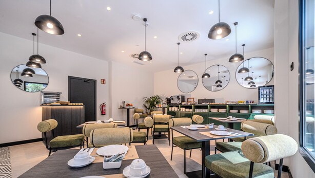 Un espace de restauration moderne avec des tables et des chaises rondes, un éclairage suspendu et une vue sur la ville grâce à de grandes fenêtres.