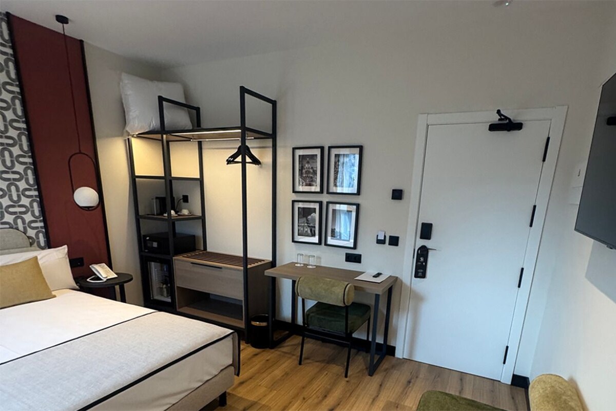 Une chambre d’hôtel de taille réduite, comprenant un lit, un bureau, une chaise, une armoire et une porte.