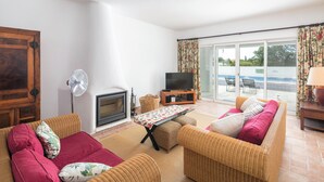 A living room with wicker furniture, a fireplace, a television, and a view of a pool through large sliding glass doors. - Garden House- Pool, Self Check-in, Private Entrance (Carvoeiro)