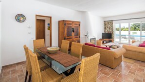 A dining area with wicker chairs and a glass table, a wooden cabinet, a television, and a sofa with a view of the pool. - Garden House- Pool, Self Check-in, Private Entrance (Carvoeiro)
