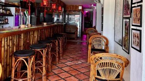 Un bar con sillas de mimbre, suelo de baldosas y una barra con varios artículos.