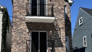 A two-story brick house with a garage, a balcony, and a staircase leading to the second floor.