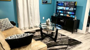 A living room with a leather sofa, a glass coffee table, a TV on a black stand, and a blue wall.