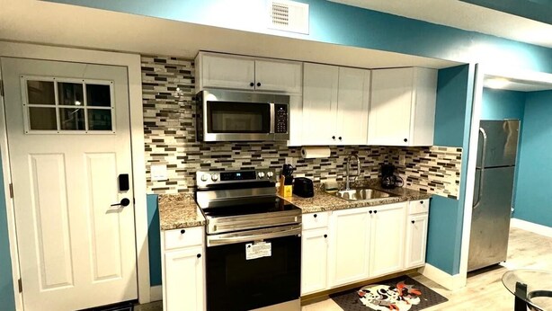 A modern kitchen with white cabinets, a stainless steel microwave, and an oven.