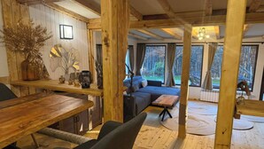 A cozy cabin interior with a dining area, a sofa, and a view of the forest through large windows. - Villa Yarema Mountain Relax With Hot Jacuzzi & Sauna (Samokov)