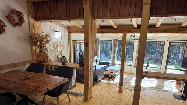 A spacious room with a wooden floor, a dining table with chairs, a sofa, and a large window offering a view of the outdoors. - Villa Yarema Mountain Relax With Hot Jacuzzi & Sauna (Samokov)