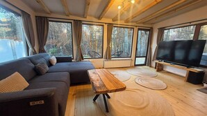 A cozy living room with a sofa, a wooden coffee table, and a TV. Large windows offer a view of the outdoors. - Villa Yarema Mountain Relax With Hot Jacuzzi & Sauna (Samokov)
