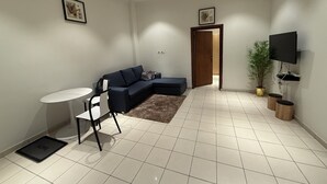 A modern living room with a sectional sofa, a small round table, and a TV mounted on the wall. - Mayama airport apartment (Accra)
